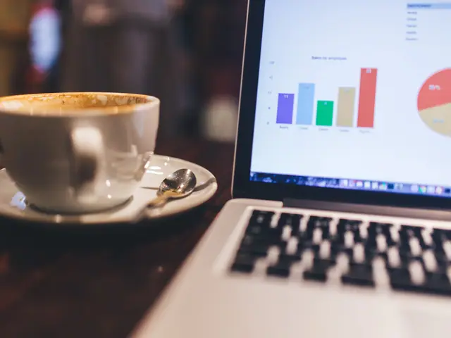Xícara de café ao lado de um notebook com um gráfico de barras na tela